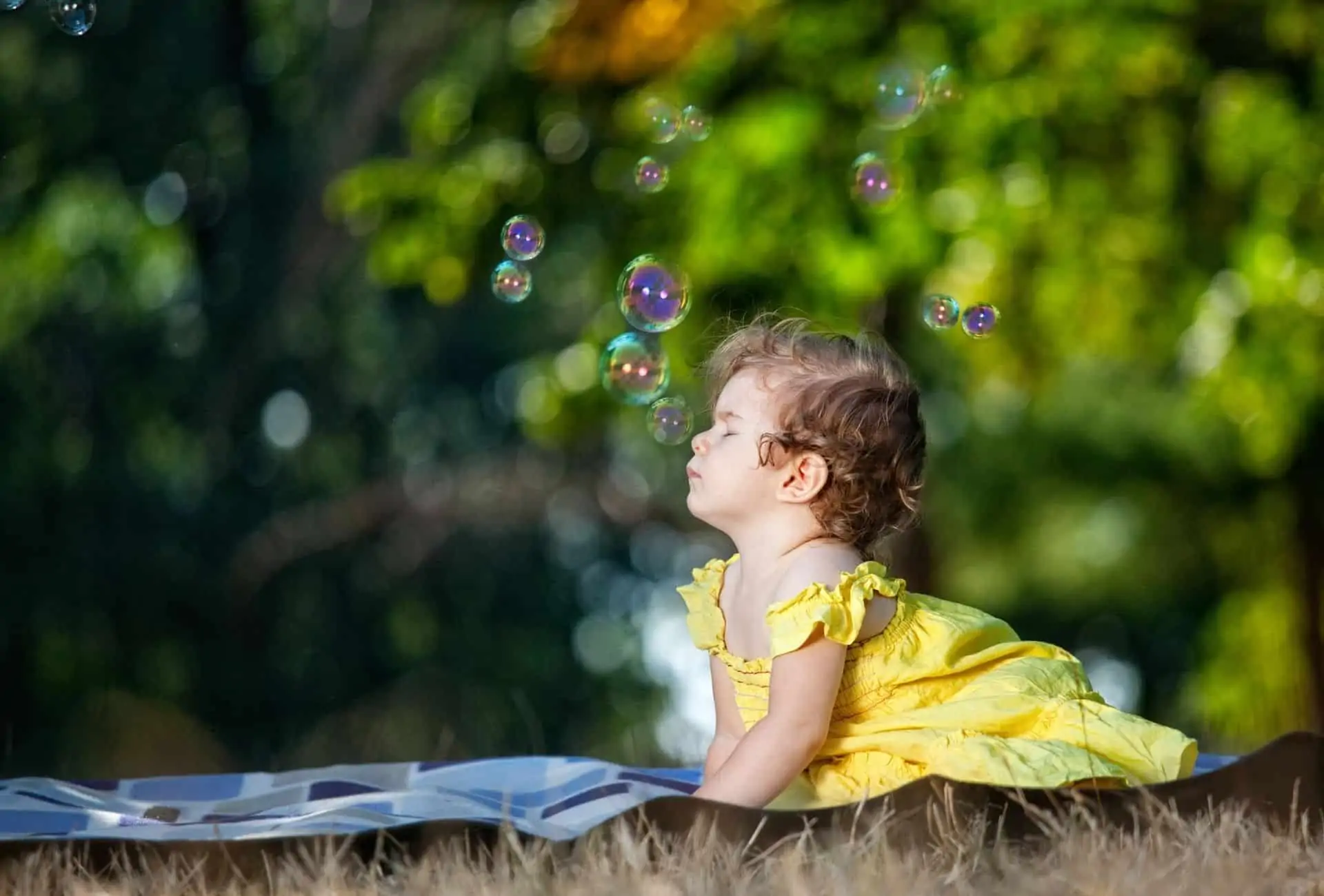 Baby girl in yellow dress looking at bubbles