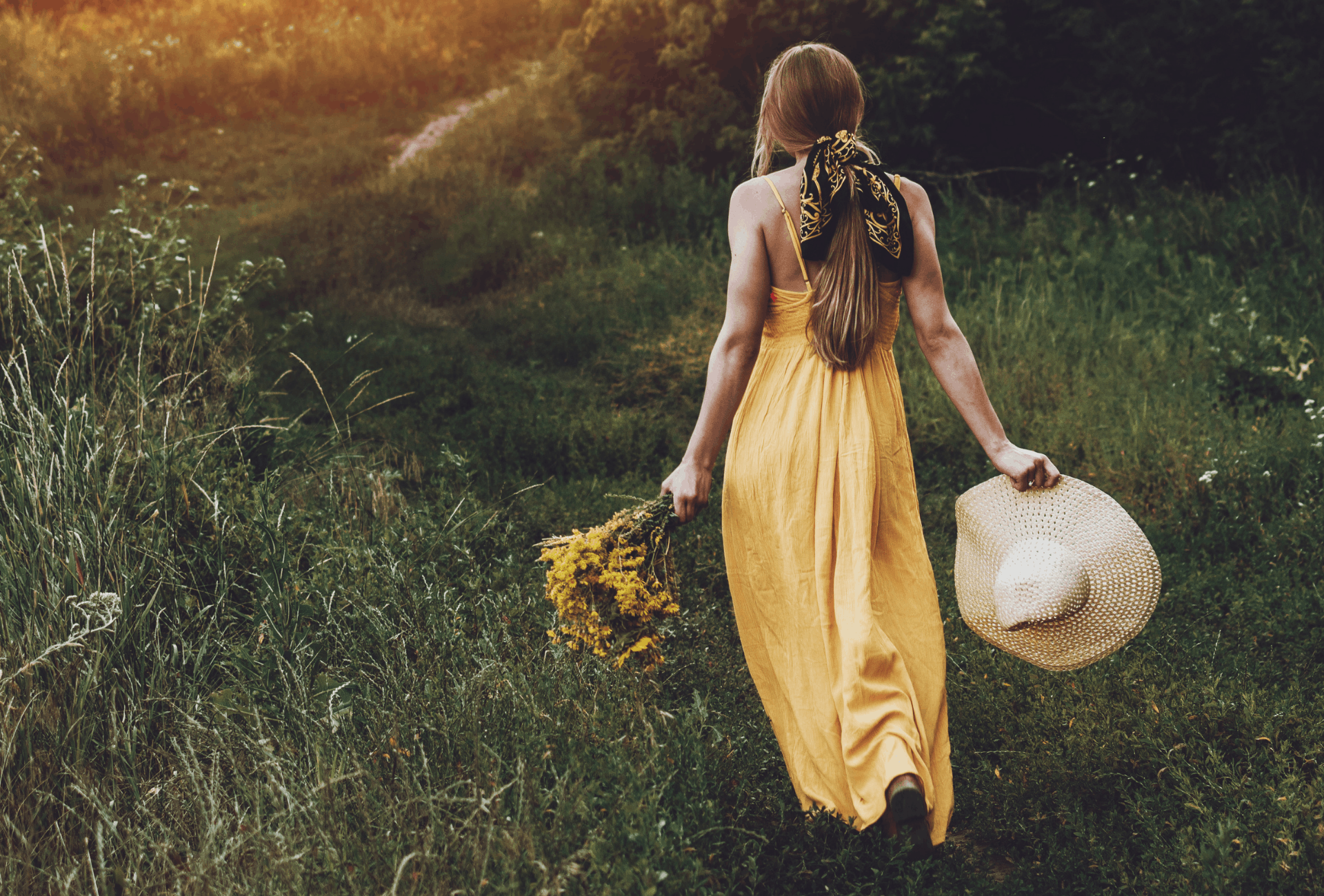 Woman in a yellow dress walking through a green field.