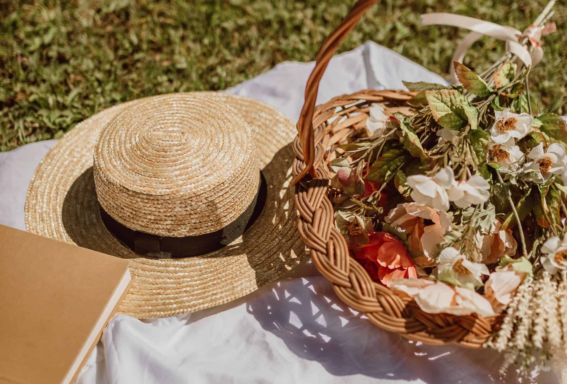 Flowers and a straw hat lying on a picnic blanket.