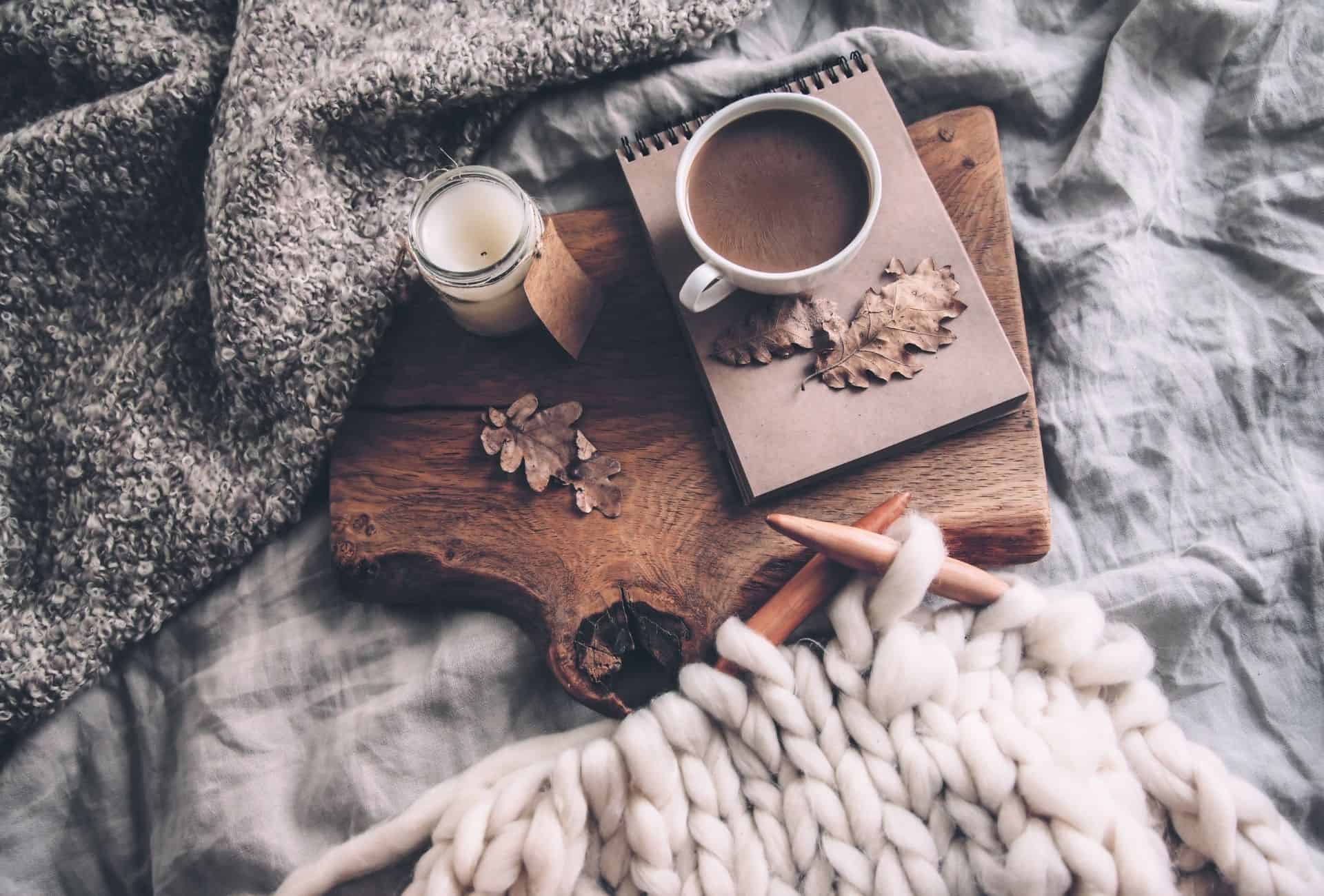 Hot chocolate and candle sitting on bed with cozy knitted blanket.